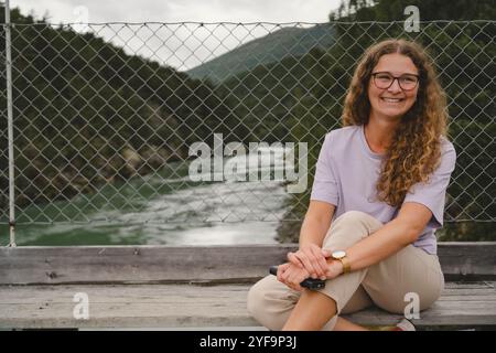 Smiling young woman sitting on boardwalk against fence Stock Photo