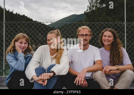 Smiling mother and father with daughters sitting against fence Stock Photo