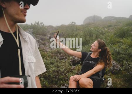 Midsection of young man with female friend taking selfie in background during hiking Stock Photo