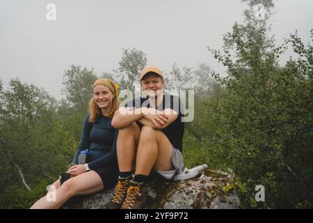 Portrait of smiling young couple sitting on rock during foggy weather Stock Photo
