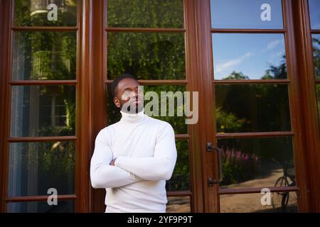 Smiling young man standing with arms crossed near door Stock Photo