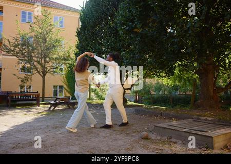 Young man spinning woman while dancing in building garden Stock Photo