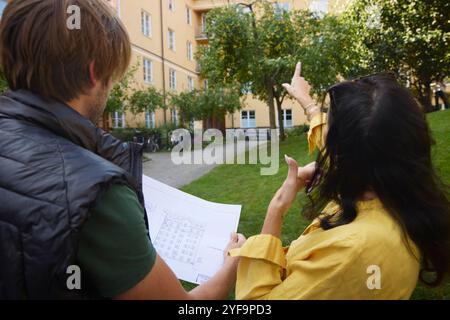 Rear view of female architect pointing while male colleague examining blueprint in garden Stock Photo