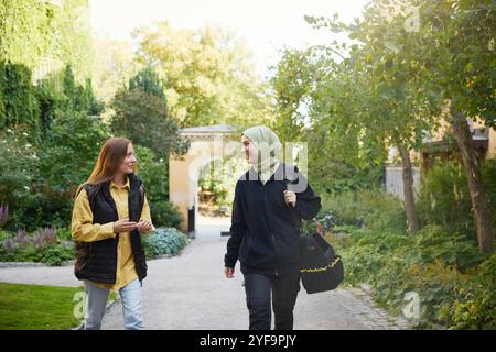 Happy repairperson in hijab talking with female resident while walking on footpath Stock Photo