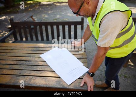 High angle view of male architect in reflective clothing examining blueprint kept on table Stock Photo