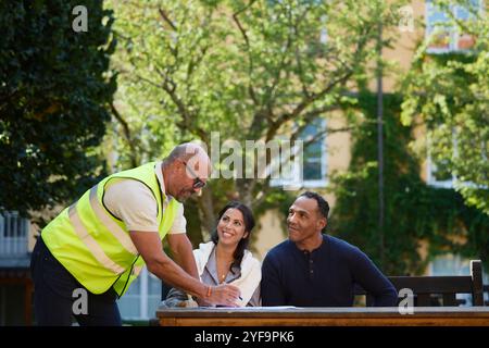 Side view of smiling male architect in reflective clothing talking with couple in garden Stock Photo