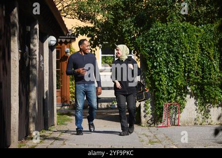 Happy male and female friends discussing while walking on footpath outside building Stock Photo