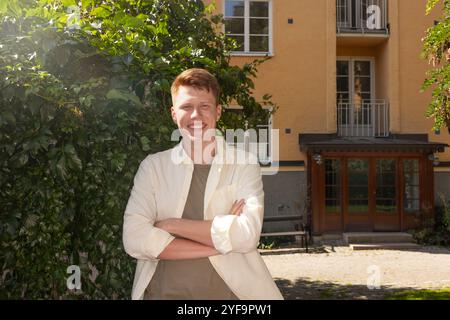 Portrait of smiling young man with crossed arms standing against building entrance Stock Photo