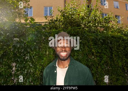 Mischievous young man with closed eyes against plants covered wall Stock Photo