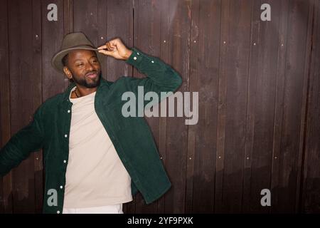 Smiling young man tipping hat against brown wall Stock Photo