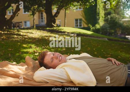 Portrait of smiling young man resting on mat in park Stock Photo