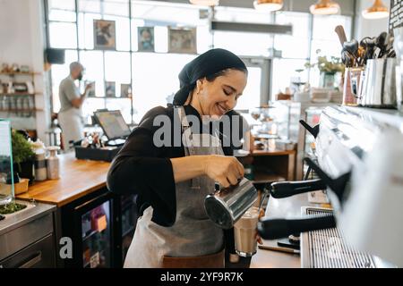 Smiling female barista making coffee while working in cafe Stock Photo
