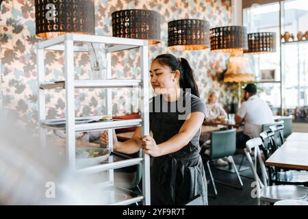 Smiling waitress pushing serving cart in cafe Stock Photo