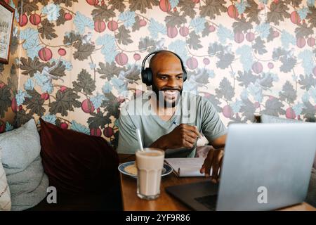 Smiling man wearing headphones while using laptop in cafe Stock Photo