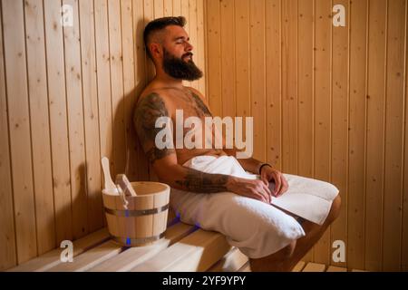 Adult man is relaxing at sauna. Bearded man is sitting in sauna and enjoying healthy treatment. Stock Photo