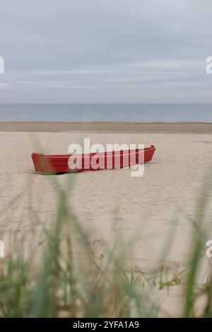 Red boat on a sandy beach against moody sky Stock Photo