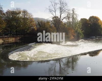 Pulteney weir, in spate after heavy rain with autumn trees behind, reflected in the waters of the River Avon. Bath, Somerset. Tourist attractions. Stock Photo