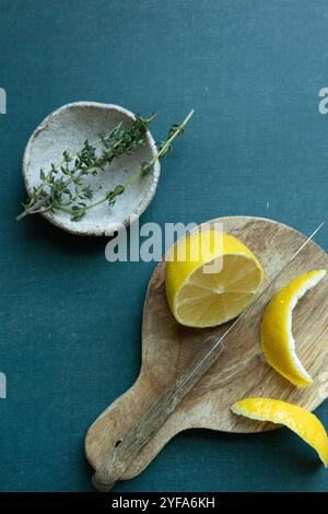Sliced lemon and thyme on rustic board against green background Stock Photo