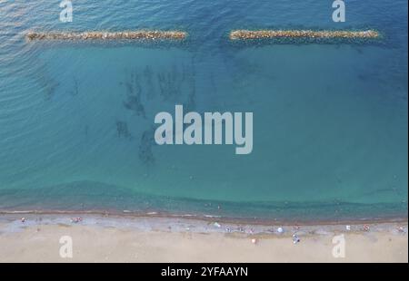 Aerial view from flying drone of people resting on the beach in Paphos Cyprus, Breakwater sea wall to protect beach from waves Stock Photo