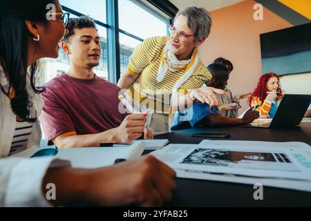 A college lecturer engaging with students, explaining concepts in a classroom. The diverse group gathers around a table, fostering collaboration and a Stock Photo
