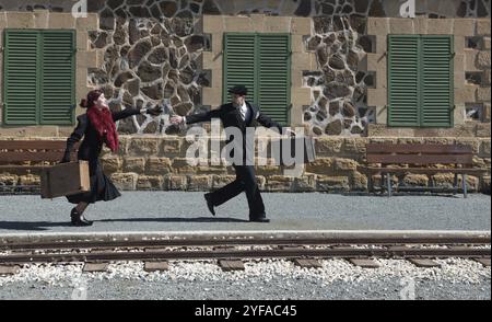 Young couple with vintage suitcase running fast outside a train station to catch the last train for journey Stock Photo