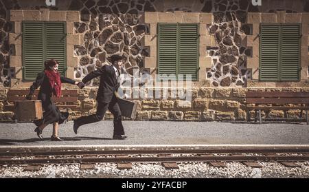 Young couple with vintage suitcase running fast outside a train station to catch the last train for journey Stock Photo