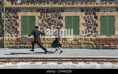 Young couple with vintage suitcase running fast outside a train station to catch the last train for journey Stock Photo