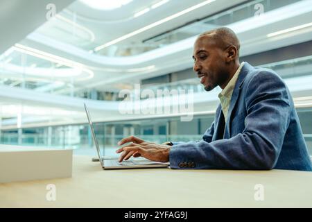 Professional businessman working on a laptop in a modern, bright office. The setting is corporate, with sleek architecture and natural lighting. He ap Stock Photo