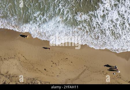 Aerial drone point of view of people walking on sand in a beach. Stormy waves idyllic beach in winter Stock Photo