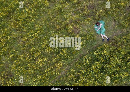 Overhead view of woman laying down on blooming meadow grass field. Spring time outdoor Stock Photo