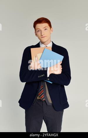 A confident student showcases his fashionable winter attire while holding colorful notebooks in a studio. Stock Photo