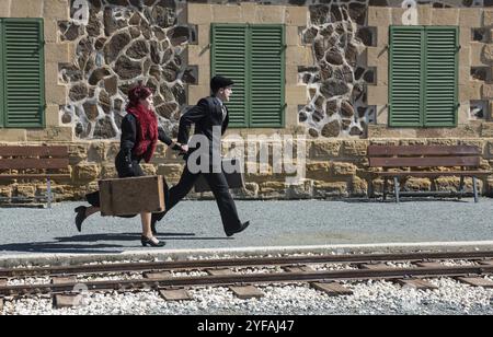 Young couple with vintage suitcase running fast outside a train station to catch the last train for journey Stock Photo