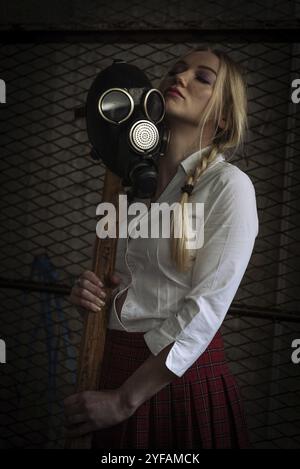 Caucasian woman holding gas protective mask and axe in an underground warehouse Stock Photo