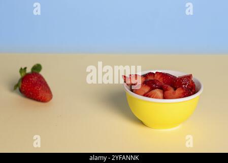 Fresh red slices of strawberries on bowl against yellow and blue background Stock Photo