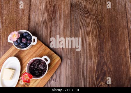 Top view of a rustic breakfast with toast and blueberry jam on a cutting board, next to a butter dish on a dark wooden table Stock Photo