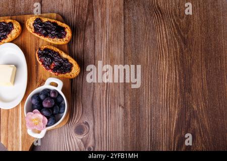 A close-up of toast with blueberry jam on a wooden board, next to a butter dish, on a dark wood table, creating a cozy breakfast feel Stock Photo