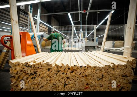 A worker operates a computerized machine in a woodworking factory, processing large wooden beams in an industrial setting Stock Photo