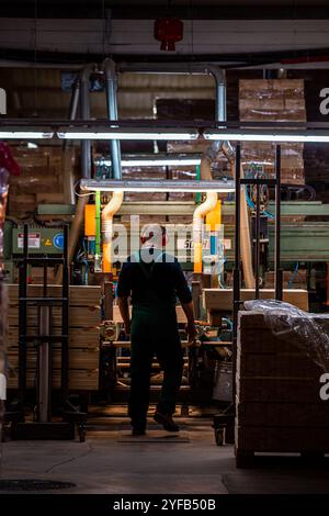 A worker operates a computerized machine in a woodworking factory, processing large wooden beams in an industrial setting Stock Photo