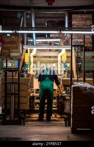 worker operates a computerized machine in a woodworking factory, processing large wooden beams in an industrial setting Stock Photo