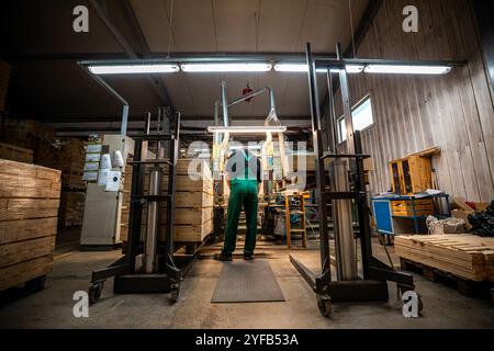 A worker operates a computerized machine in a woodworking factory, processing large wooden beams in an industrial setting Stock Photo