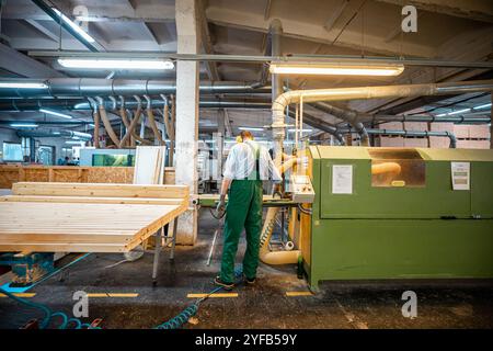 worker operates a computerized machine in a woodworking factory, processing large wooden beams in an industrial setting Stock Photo