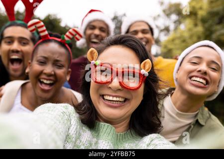 Taking selfie, wearing festive hats, multiracial friends celebrating christmas outdoors Stock Photo