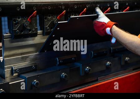 Close-up of a worker's gloved hand adjusting metal components in an industrial press machine, emphasizing precision and control. Stock Photo
