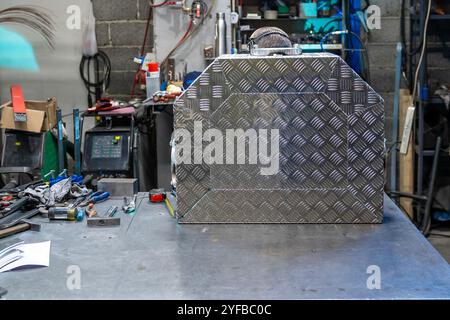 Side view of a checkered metal box on a workbench in a workshop, with various tools and equipment scattered around. Stock Photo