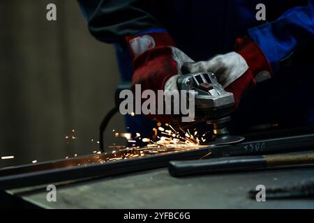 Craftsman using an angle grinder, creating bright sparks while working on a metal frame in the workshop. Stock Photo