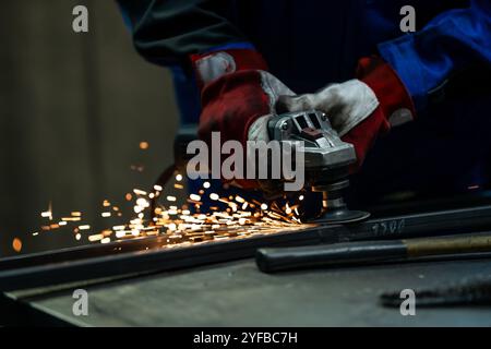 Craftsman using an angle grinder, creating bright sparks while working on a metal frame in the workshop. Stock Photo