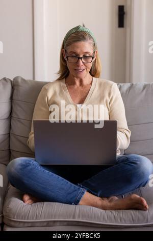 senior woman using laptop at home, sitting comfortably on sofa, smiling Stock Photo