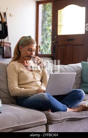 senior woman using laptop at home, thinking and holding glasses thoughtfully Stock Photo