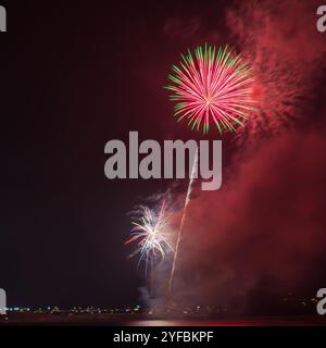 Public firework display over Coney Beach in Porthcawl, Wales, with colourful bursts lighting the night sky during a seasonal celebration. Stock Photo