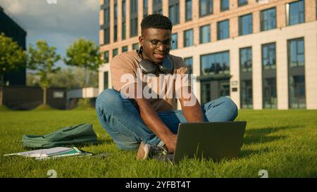 Happy smiling African American man university college academy student guy teenager male studying homework online on grass meadow in park study Stock Photo